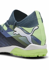 Calzado Puma con una parte superior texturizada en azul marino, acentos en verde y amarillo, patrón a rayas y un logo blanco en el talón. Suela de goma para tracción.