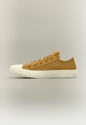 Baskets basses en toile beige avec semelle et bout en caoutchouc blanc, lacets beige assortis, présentées de profil sur un fond neutre.