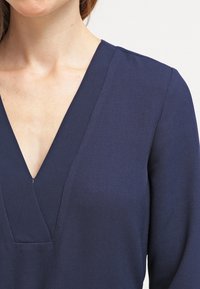 Top azul marino con diseño de escote en V profundo, tela texturizada con un patrón sutil y hombros estructurados.