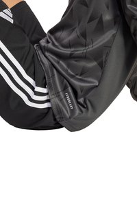 Schwarzes Sportshirt mit geometrischen Mustern, AEROREADY-Label, Adidas-Branding und weißen Akzenten an den Ärmeln. Glattes, leichtes Gewebe.