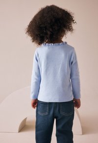 Hellblauer Pullover mit gerafftem Ausschnitt, kombiniert mit dunkelblauen Jeans. Der Pullover hat ein strukturiertes Muster.