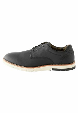 Zapato de cuero negro con un acabado suave, puntera redonda, suela blanca en contraste y detalles de textura en la parte superior. Cintas y forro interior de cuadros.