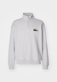 Sudadera de forro polar gris con cuello de media cremallera y puños de canalé, que presenta un logo de cocodrilo bordado en verde en el lado izquierdo del pecho.