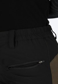 Zwarte broek met een elastische tailleband, voorzien van een ritszak en een contrasterend kaki paneel aan de zijkant. Glad textuur, functioneel ontwerp.