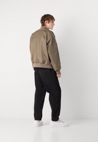 Veste bomber kaki avec une finition lisse, des poignets et un ourlet côtelés, associée à un pantalon noir ample et des baskets blanches.