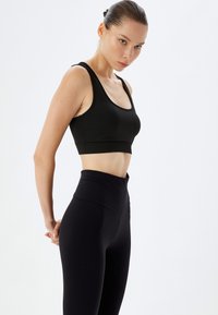 Zwarte sportieve crop top met brede banden en ondersteunende elastiek, gecombineerd met hoge, zwarte leggings van een gladde, rekbare stof.