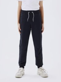 Navyblå joggebukser med snor i midjen, slank design, sidelommer og tettsittende mansjetter; kombinert med lyse sneakers.