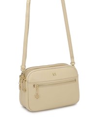 Béžová crossbody taška vyrobená z textúrovanej kože, s použitím zlatej kovania, dvoma zipsovými priehradkami a dekoratívnymi príveskami.