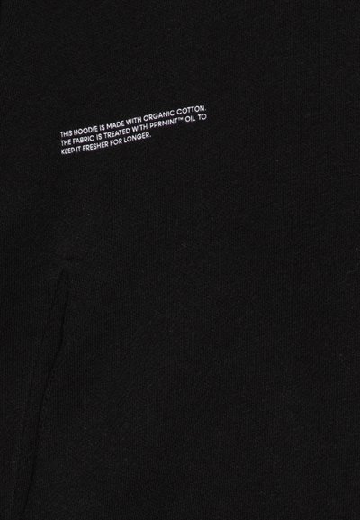 Manta preta feita com algodão orgânico. Apresenta uma textura suave, bolso lateral e pequenos detalhes em texto branco sobre o tratamento do tecido para frescura.