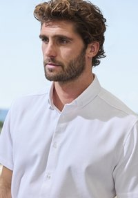 Weißes Kurzarmhemd mit Button-Down-Kragen, ausgestattet mit einem strukturierten Stoff und drei Knöpfen entlang der Knopfleiste.