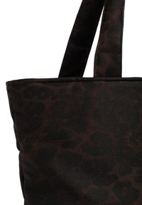 Gros plan sur un sac cabas marron foncé avec un motif léopard noir et des anses en tissu.