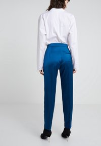 Blue satin trousers with a tailored fit, high waist, and side pockets. Paired with a long-sleeve white shirt and black heeled booties.