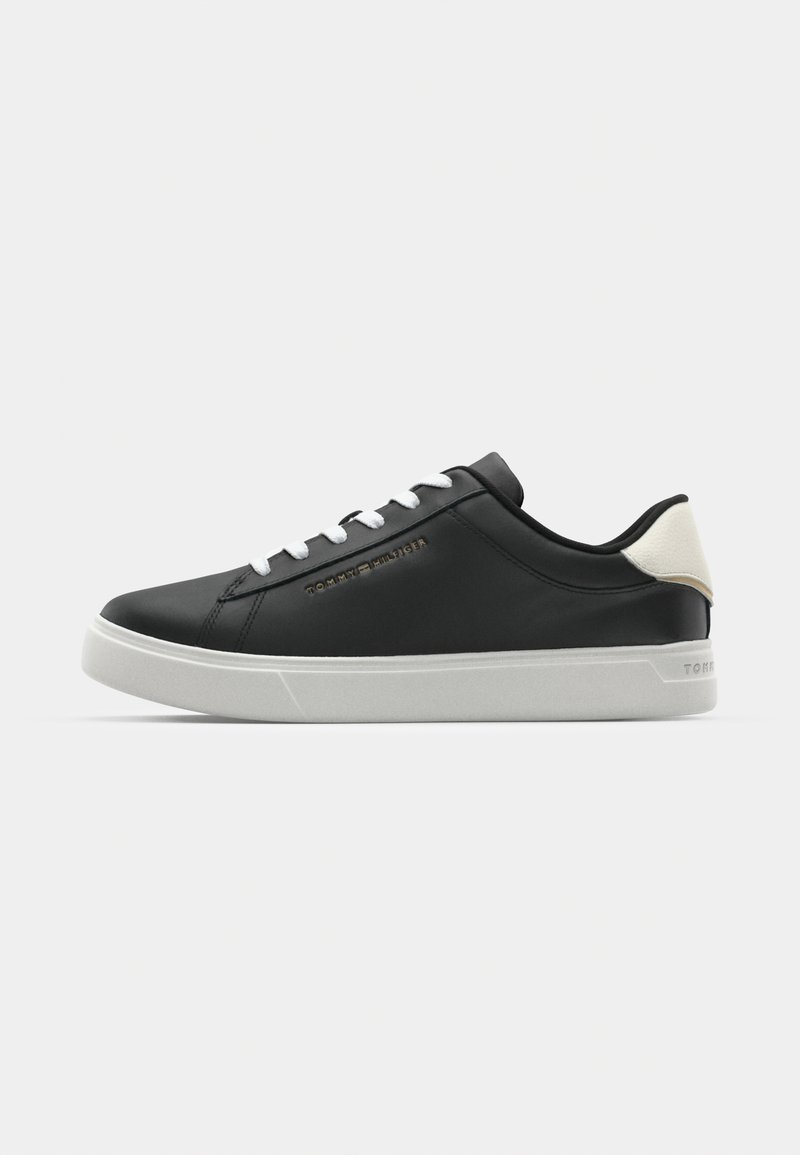 Zapatillas de cuero sintético negro con cordones blancos, suela de goma, detalle del logo en dorado y acento de talón en crema contrastante.
