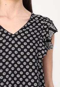 Tessuto nero con piccoli motivi a fiori bianchi, dotato di scollo a V e maniche arricciate con dettagli intricati. Texture morbida.