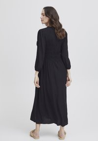 Schwarzes langärmeliges Kleid mit gekräuseltem Oberteil, fließendem Rock und lockerer Passform. Verfügt über einen weichen Stoff und eine Taillenbetonung für eine formende Silhouette.
