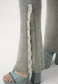 Mallas de punto grises con cierres de botones laterales en hardware plateado. Combinadas con zapatos de plataforma azules con textura de denim y punta abierta.