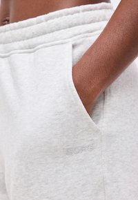 Χέρι με σκουρόχρωμο δέρμα που ξεκουράζεται στην τσέπη ανοιχτόχρωμου γκρι παντελονιού φόρμας με ελαστική μέση και διακριτικό λογότυπο "BORG".