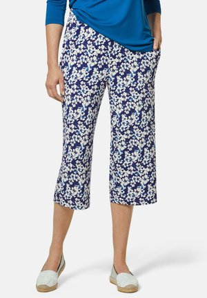 Pantalons capri fleuris en bleu marine, ornés de motifs floraux blancs et bleus, en tissu doux et dotés de poches latérales. Associés à des chaussures à enfiler de couleur claire.