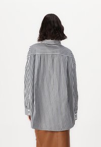 Maglietta a righe bianche e nere con una vestibilità rilassata, maniche lunghe e un design con yoke posteriore. Il tessuto appare leggero e liscio.
