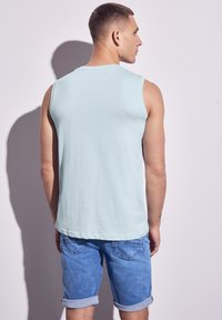 Světlemodrá bezrukávová košile vyrobená z měkké látky, kombinovaná s modrými denimovými šortkami. Šortky mají ohrnuté lemy. Žádné viditelné vzory ani akcenty.