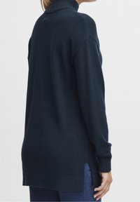 Granatowy sweter z golfem o luźnym kroju, długimi rękawami, bocznymi rozcięciami przy krawędzi i miękką dzianinową fakturą.