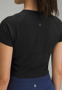 Zwart sporttop met korte mouwen, met een gladde textuur en een subtiele logo op de rug. Gecombineerd met blauwe high-waisted leggings.