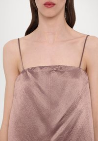 Brun satengcamisole med tynne stropper, med en jevn tekstur og subtil glans. Enkelt design med samlet hals og rett silhuett.