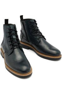 Skórzane botki za kostkę w ciemnym niebieskim kolorze, z wiązaniem z przodu i suwakiem z boku. Charakterystyczna brązowa podeszwa o teksturowanym wykończeniu i kontrastowym obszyciu.