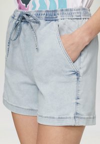 Jasnoniebieskie szorty dżinsowe z elastycznym pasem, z zamknięciem na sznurek i kieszeniami bocznymi. Charakteryzują się kontrastowym ściegiem oraz luźnym krojem.