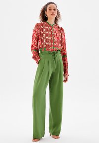 Röd blus med blommönster och gröna accenter, ihop med högmidjade gröna byxor. Slät textur, lös passform och knytning i midjan.