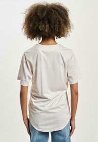 Lys beige kortermet skjorte med vertikale blå striper, rund hals og buet nederkant. Laget av glatt, lett stoff.