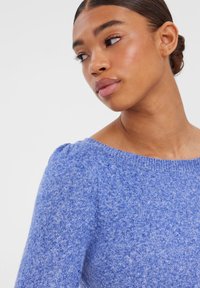 Pull en tricot bleu avec un large col et des manches trois-quarts. Tissu doux et texturé avec un motif subtil mélangé.