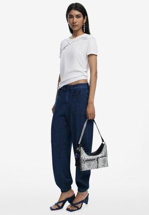 Weißes T-Shirt mit gesticktem Detail, dunkelblaue Jeanshose und blaue Riemchen-High Heels. Silberne Taschen aus Schlangenleder mit schwarzen Akzenten.