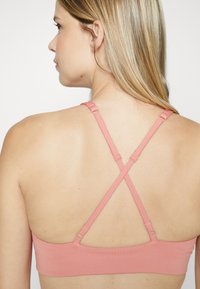 Sostén deportivo rosa con tirantes ajustables en forma de cruz, fabricado en tela suave y con detalles de costura sutiles. Diseñado para comodidad y soporte.