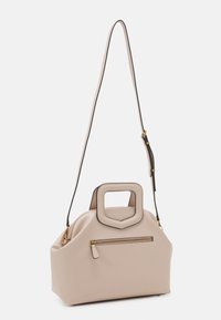 Beige skuldertaske lavet af glat materiale, med et firkantet håndtag, justerbar rem og en lynlåslomme på forsiden. Gyldne hardware detaljer.