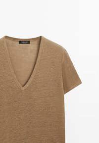 T-shirt marron à manches courtes avec col en V, en tissu doux texturé, avec une petite étiquette noire Massimo Dutti à l'intérieur du col.