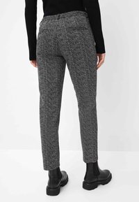 Graue Hahnentritt-Hosen mit taillierter Passform, dehnbarem Bund, seitlichen Taschen und strukturiertem Stoff. Kombiniert mit schwarzen Ankle-Boots.