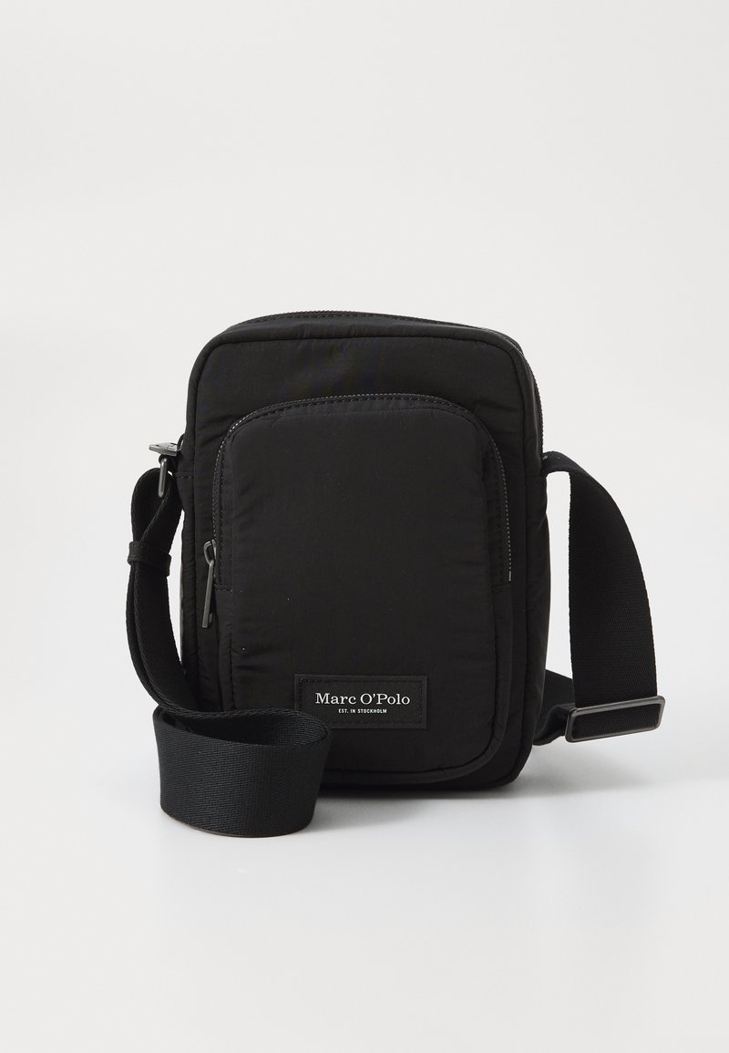 Svart nylon crossover-veske med quiltet design, justerbar stropp og frontlommes med glidelås samt et merke-etikett nederst.