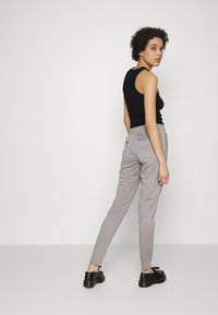Calças cinzentas justas com cintura elástica, dois bolsos traseiros e sapatos pretos com atacadores. Design simples, textura suave e silhueta curvada.