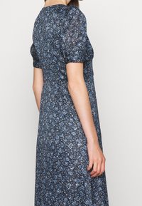 Vestido de estampado floral azul con mangas abullonadas y cintura ceñida. La tela tiene un acabado texturizado, con una silueta larga y fluida.
