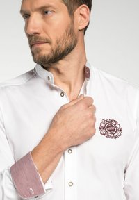 Witte Overhemd met rode geruite manchetten, voorzien van een bordeauxrood geborduurd logo op de borst. Soepele stof met een gestructureerde kraag.