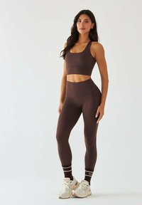 Brązowy sportowy krótki top i leginsy z wysokim stanem wykonane z elastycznego materiału. Dopełnieniem stroju są białe i brązowe skarpetki w paski oraz jasne sneakersy.