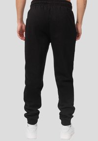 Persona vistiendo pantalones jogger negros y zapatillas Nike Air blancas, vista desde atrás contra un fondo gris liso.