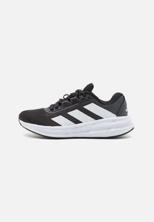 Black athletic shoe with a textured fabric upper, featuring three white stripes on the side, a white midsole, and a rubber outsole.