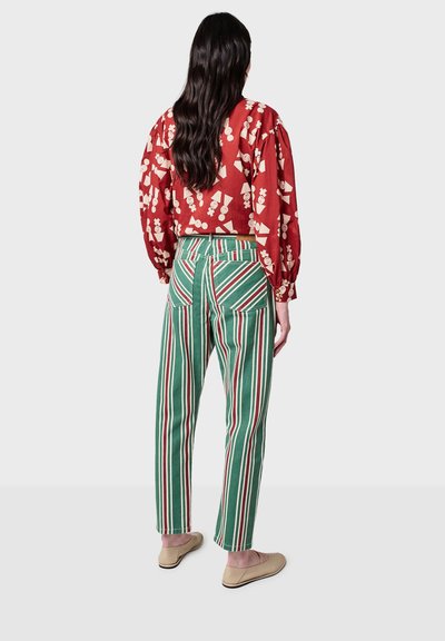 Cropped top floreale rosso abbinato a pantaloni a vita alta a righe verdi e bianche con tasche posteriori. La modella indossa delle slip-on color beige.