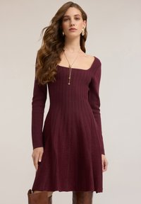 Weinrotes, geripptes Kleid mit quadratischem Ausschnitt und langen Ärmeln, das unterhalb der Taille ausgestellt ist, gefertigt aus weichem, strukturiertem Stoff.