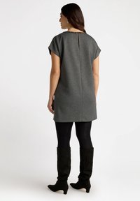 Graues Kurzarmkleid mit taillierter Form, ausgestattet mit einem Schlüsselloch-Ausschnitt und Perlenakzenten, kombiniert mit schwarzen Strumpfhosen und kniehohen Stiefeln.