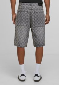 Graue Denim-Shorts mit strukturiertem Muster, ausgestattet mit zwei Gesäßtaschen und knielangem Design. Tragen Sie dazu weiße Socken und Sneaker.