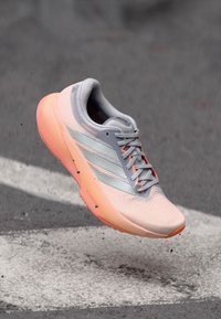 Sneaker mit hellpinkem Obermaterial und oranger Sohle, mit silbernen Streifen, strukturiertem Stoff und kontrastierender Schnürung. Leichtes Design, minimalistische Form.