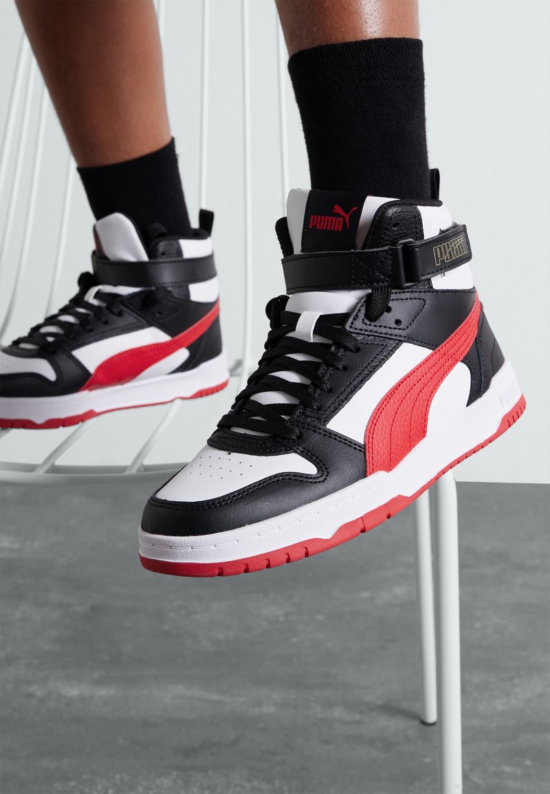 Sneaker alte in pelle nera con accenti rossi e dettagli bianchi, dotate di suola in gomma, lacci e un strap in velcro.